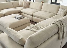 a large sectional couch in a living room with pillows on the back and an ottoman next to it