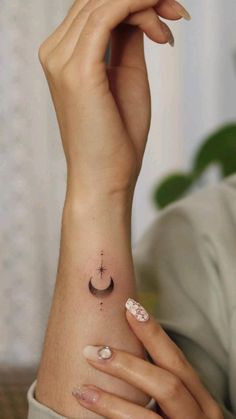 a woman's hand with a small tattoo on her left wrist and the moon behind her arm