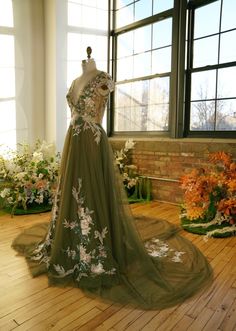 a dress is on display in front of a window with flowers and greenery around it