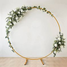 a circular wooden stand with flowers and greenery on it, against a white wall