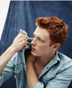a young man with red hair is holding his cell phone to his ear and looking off into the distance