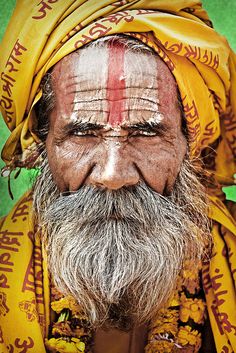 an old man with purple and yellow painted on his face, wearing a turban