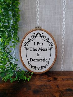 i put the mess in domestic cross stitch pattern on a wooden hoop with greenery next to it