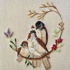 two birds sitting on top of a branch with flowers in the middle and one bird perched on it's back