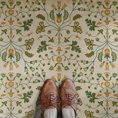 a person wearing brown shoes standing in front of a wallpapered floor with green and yellow flowers