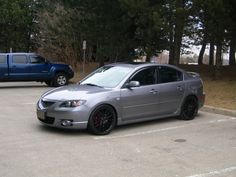 a silver car parked in a parking lot next to another blue truck and some trees