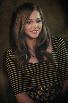 a woman with long hair wearing a striped shirt and black skirt smiling at the camera