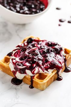 a waffle topped with blueberry sauce and whipped cream on a marble counter top