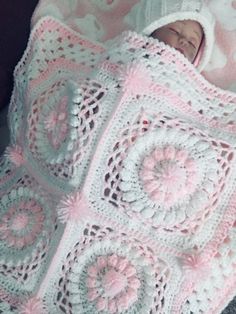 a baby wrapped up in a crochet blanket with pink and white flowers on it