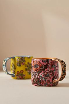 two coffee mugs sitting next to each other on a white counter top, one is decorated with flowers and the other has leopard print