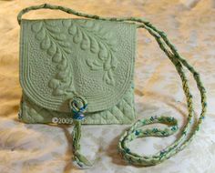 a green handbag sitting on top of a bed next to a white blanket with a rope