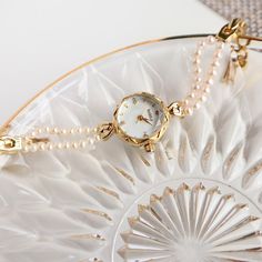 a watch sitting on top of a glass plate with pearls around the edges and a chain attached to it