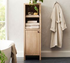 a wooden cabinet next to a bathtub with towels on it and a potted plant in the corner