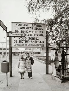 two people standing in front of a sign that says you are leaving the american sector
