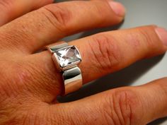 a person's hand with a silver ring on top of their finger and a white diamond in the middle