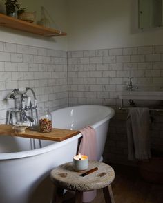 a white bath tub sitting in a bathroom next to a wooden stool with a candle on it