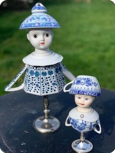 two porcelain figurines sitting on top of a black table in front of green grass