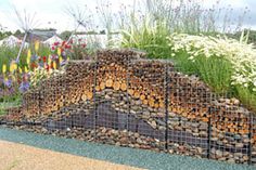 a pile of logs sitting on top of a field next to tall grass and flowers