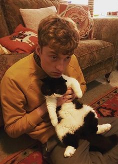 a young man sitting on the floor holding a black and white cat in his hands