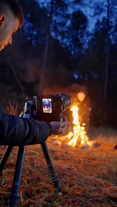 a man sitting in front of a fire holding a camera