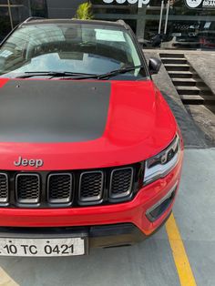 a red jeep parked in front of a building with its hood up and the name jeep on it