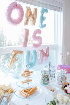 a table filled with lots of food and balloons that spell out the word one is me