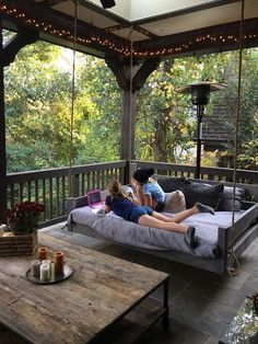two people sitting on a porch swing bed with lights strung from the ceiling above them