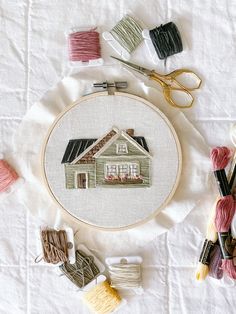 the embroidery kit is next to scissors, thread and yarn on a white tablecloth