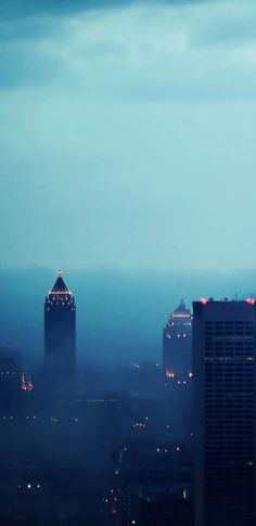 the city skyline is lit up at night with buildings in the foreground and fog on the ground