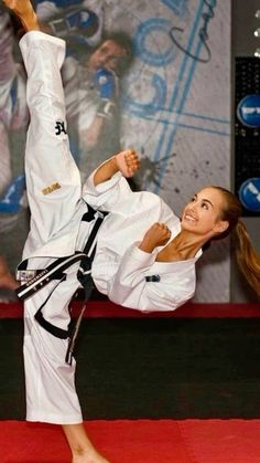 a woman doing karate moves on a red carpet in front of a wall with an advertisement behind her