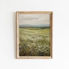 a painting hanging on the wall in front of a white wall with grass and wildflowers