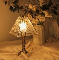 a table lamp sitting on top of a bed next to a vase filled with flowers