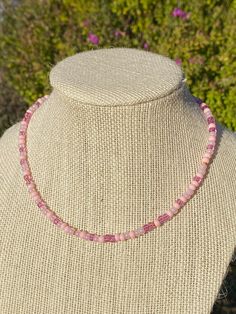 a pink necklace on a mannequin with flowers in the background