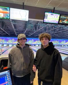 two young men standing next to each other in front of bowling alleys and television screens