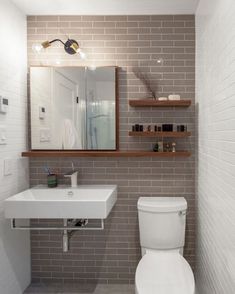 a white toilet sitting under a bathroom mirror next to a sink in a room with grey tiles on the walls