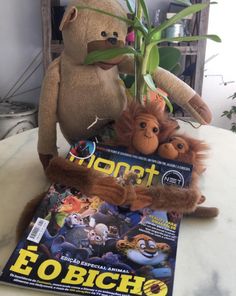 two stuffed animals sitting on top of a magazine next to a potted plant with leaves