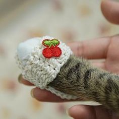 a cat's paw is holding a small crocheted hat with a strawberry on it