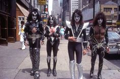 three men in black and white costumes are walking down the street with their faces painted like cats