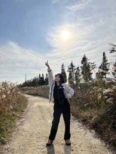 a woman standing on a dirt road with her arms in the air