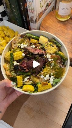 a person holding a bowl of food with corn on the cob and other foods