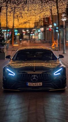 the front end of a car parked on a street at night with trees in the background