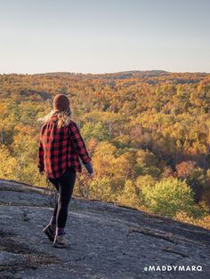 a woman walking on top of a mountain with trees in the backgrounnd