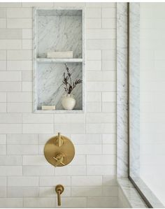 a white bathroom with gold faucet and marble wall tiles on the shower walls