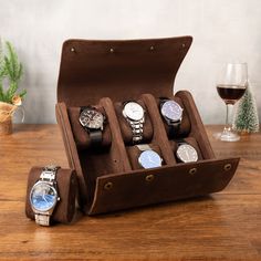 six watches in a leather case on a wooden table next to a glass of wine