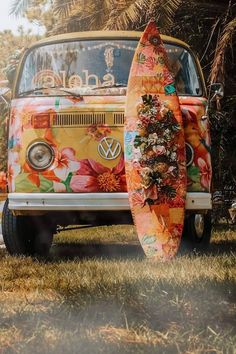 an old vw bus with flowers painted on it and two surfboards leaning against the front