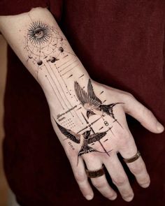 a person's hand with tattoos on it and birds flying over the top of them