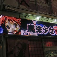 an illuminated sign with anime characters on it in front of a storefront at night