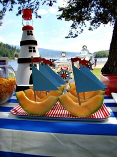 a table topped with watermelon boats and pineapples next to a lighthouse