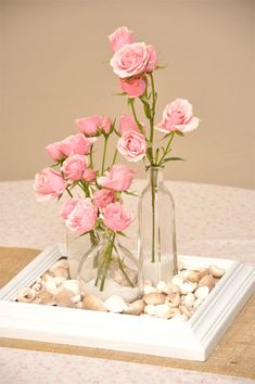 two vases filled with pink roses sitting on top of a white tray covered in rocks