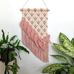 a pink and white wall hanging next to a potted plant